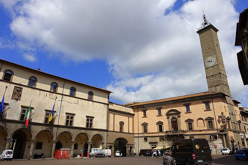 Grande piazza con palazzo del comune sulla sinistra e alto campanile che svetta sulla destra